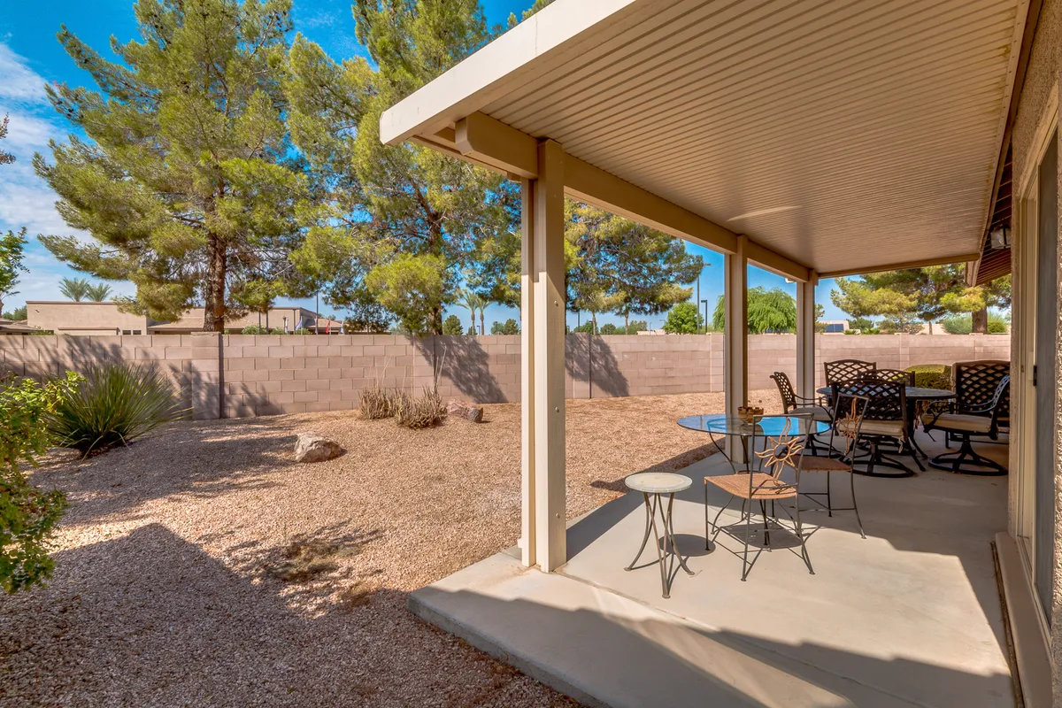 An inviting patio scene with comfortable furniture set in a landscaped garden bordered by a line of trees. The space is designed for outdoor dining, relaxation, and celebrations, inviting residents to enjoy the mild weather and community camaraderie.