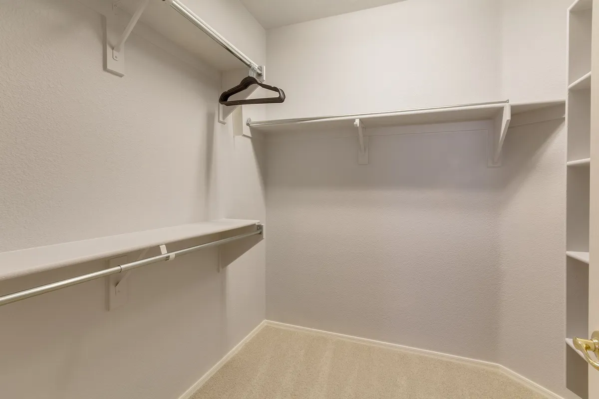 A functional walk-in closet with open shelves, hanging rods, and soft carpeting. The minimalist organization highlights ample storage space, making it easy to keep clothing and accessories tidy and accessible.