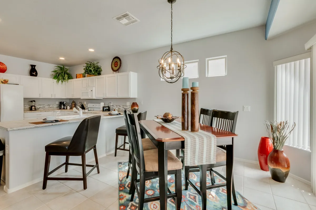 A warm, open dining area with a central table, bar stools at the kitchen island, decorative vases, and soft lighting. The setting is ideal for casual dining, entertaining guests, and morning coffee.