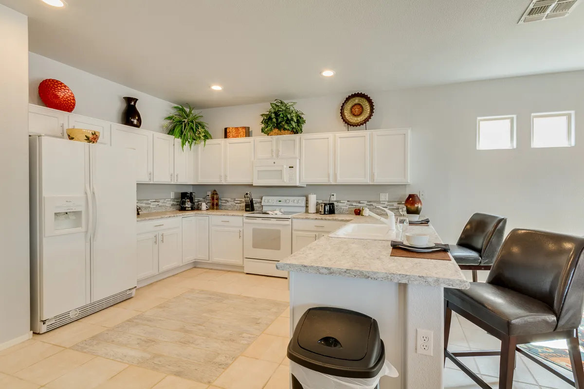 This image spotlights the remodeled kitchen, featuring pristine white cabinetry, granite countertops, bar stools for casual breakfasts, and modern appliances. Decorative plants and natural lighting further enhance the cheerful, welcoming vibe, making it easy to envision culinary adventures.