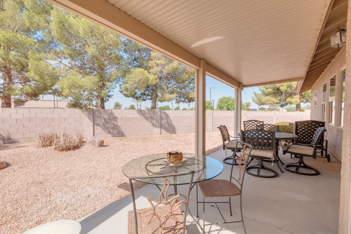 A tranquil backyard scene featuring patio furniture arranged for both lounging and dining. The surrounding yard is spacious, with well-maintained greenery creating a serene, private retreat. Sunlight filters through the trees, illuminating the relaxing outdoor space.