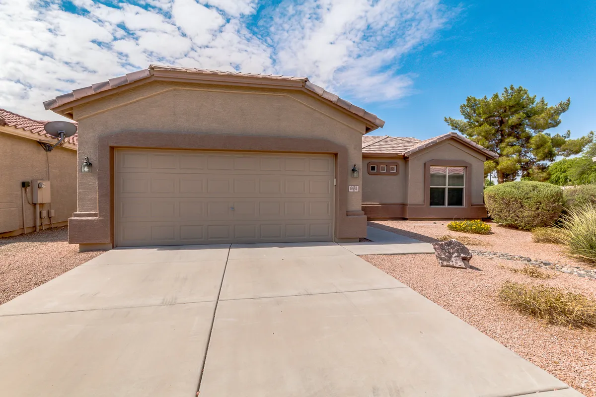 A welcoming exterior shot focused on the garage door and entrance. Lush landscaping frames the scene, while the garage is prominently featured, hinting at its spaciousness for storing cars, golf clubs, or bikes.