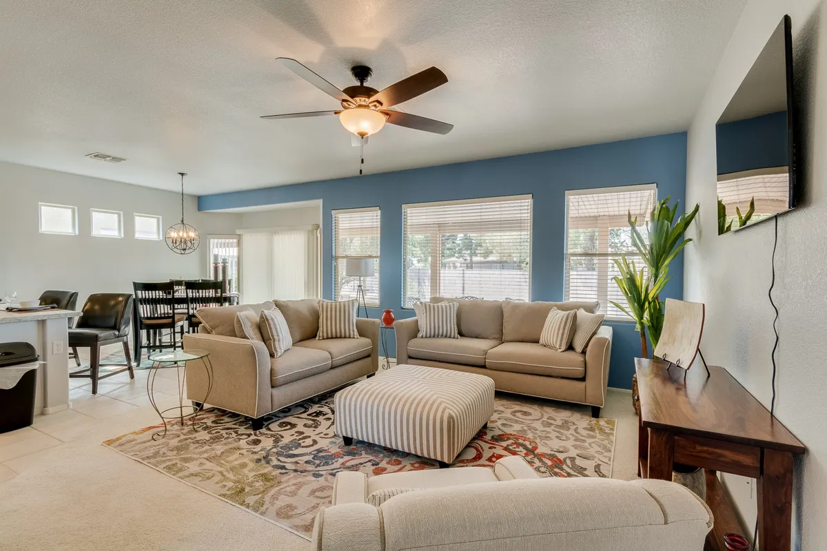 A spacious and inviting living area featuring comfortable sofas, a coffee table, stylish area rug, wall decor, and lush plants. The arrangement is ideal for socializing, relaxing, or enjoying entertainment with friends and family.
