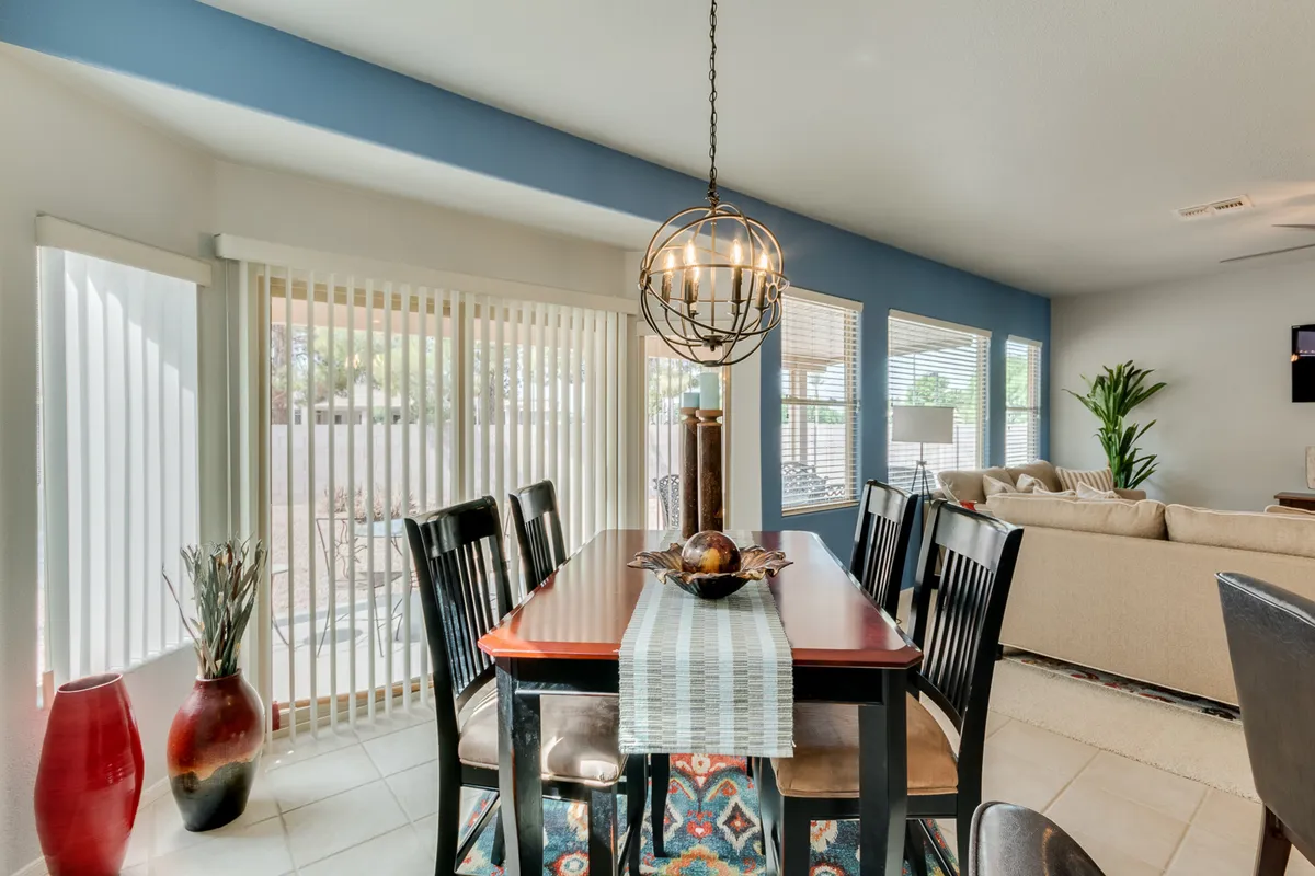 This image highlights the dining area, adorned with a stylish chandelier, decorative vases, and sliding glass doors that let in an abundance of sunlight. The living area is visible beyond, contributing to the sense of openness and connection between spaces. The décor and layout evoke a welcoming atmosphere, ideal for both lively get-togethers and quiet family evenings.